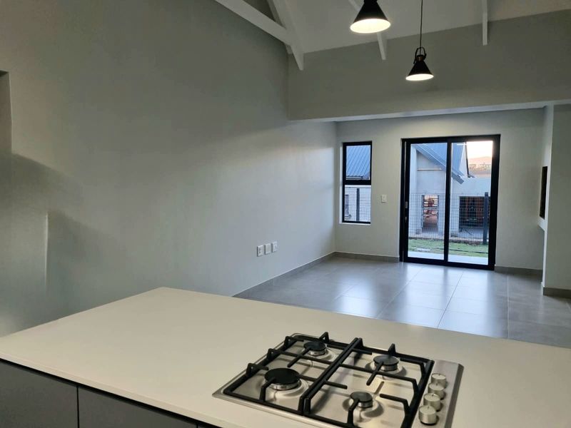 Modern open-plan living area featuring a kitchen island with a gas hob, vaulted ceilings, and large sliding doors leading to the exterior.