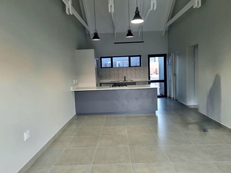 Modern open-plan kitchen and living area featuring tiled floors, exposed rafters, pendant lighting, and a sleek kitchen island with a built-in hob.