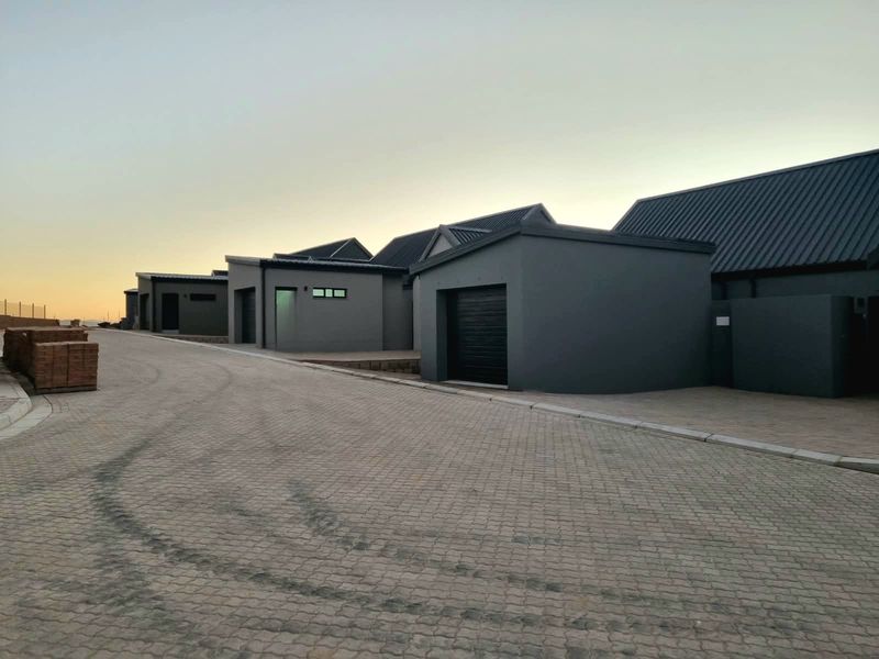 A view of the front exterior of modern cottage-style units featuring dark grey facades, metal roofing, and paved driveway access.