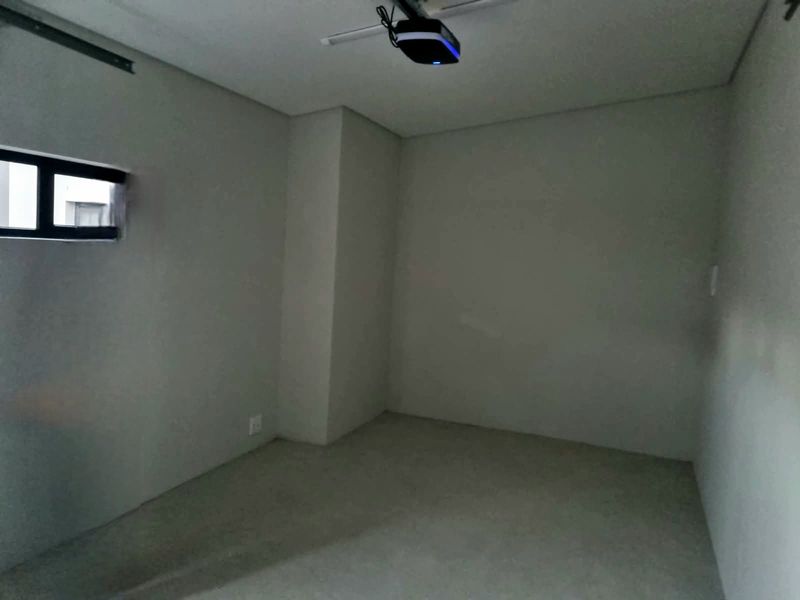 An empty, neutral-toned room featuring a ceiling-mounted projector and a small horizontal window, offering a blank canvas for various interior design possibilities.