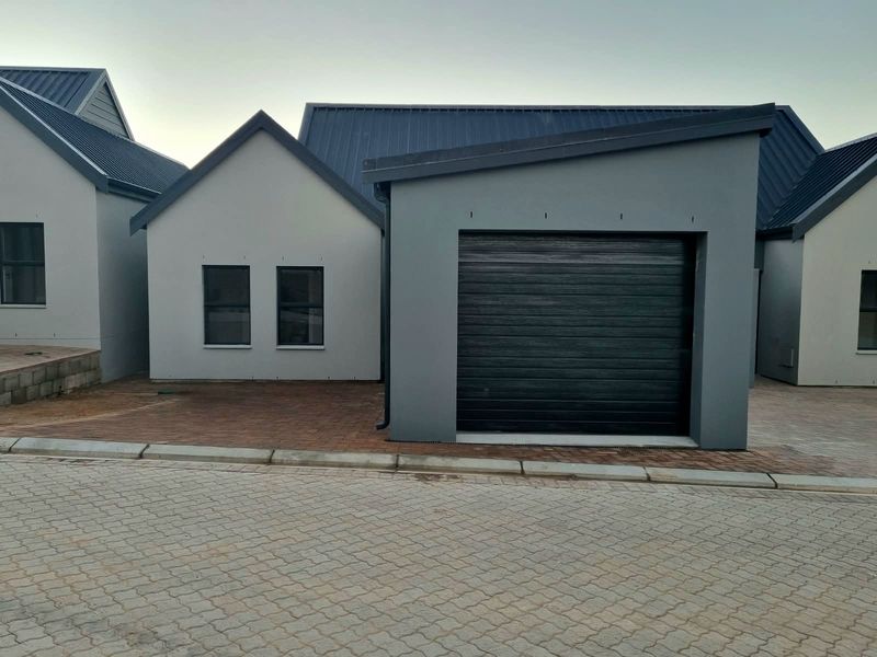 Modern cottage exterior featuring a dark metal roof, grey facade, and a single garage with a paved driveway.