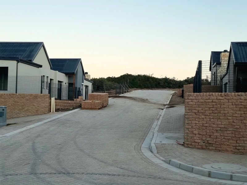 A view of a residential street in a developing estate, featuring paved driveways, brick boundary walls, and modern cottage-style homes under construction.