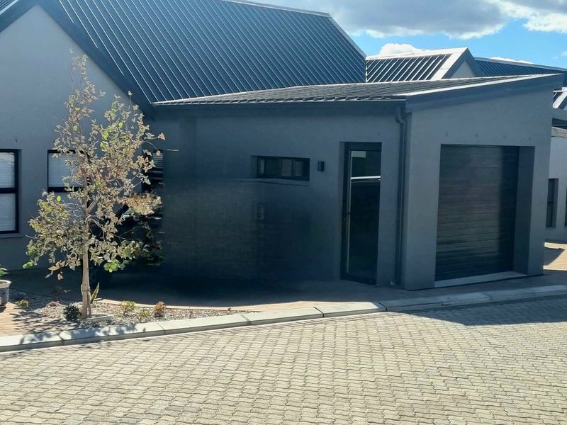 Modern cottage exterior featuring a sleek metal roof, paved driveway, and integrated garage door, presenting a clean and contemporary facade.