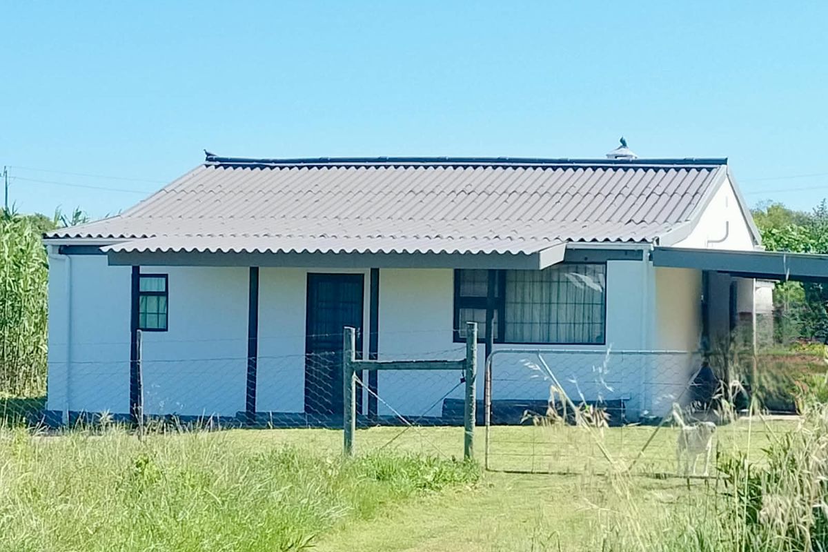 Front view of a modest farm cottage featuring a corrugated metal roof, security gates, and a fenced yard area.
