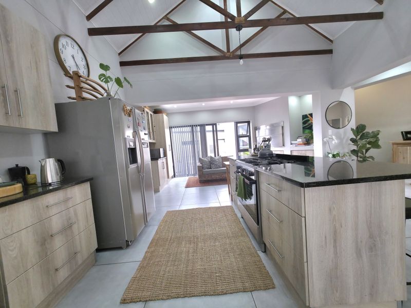 Spacious open-plan kitchen and living area featuring vaulted ceilings with exposed timber trusses, modern cabinetry, granite countertops, and a central island with gas hob.