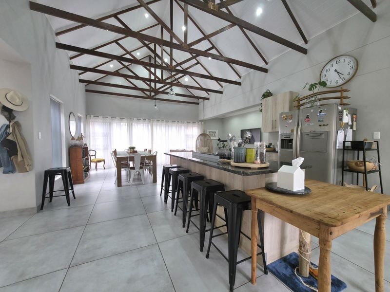 Spacious open-plan living and kitchen area featuring high vaulted ceilings with exposed timber trusses, modern tiled flooring, and a central kitchen island.