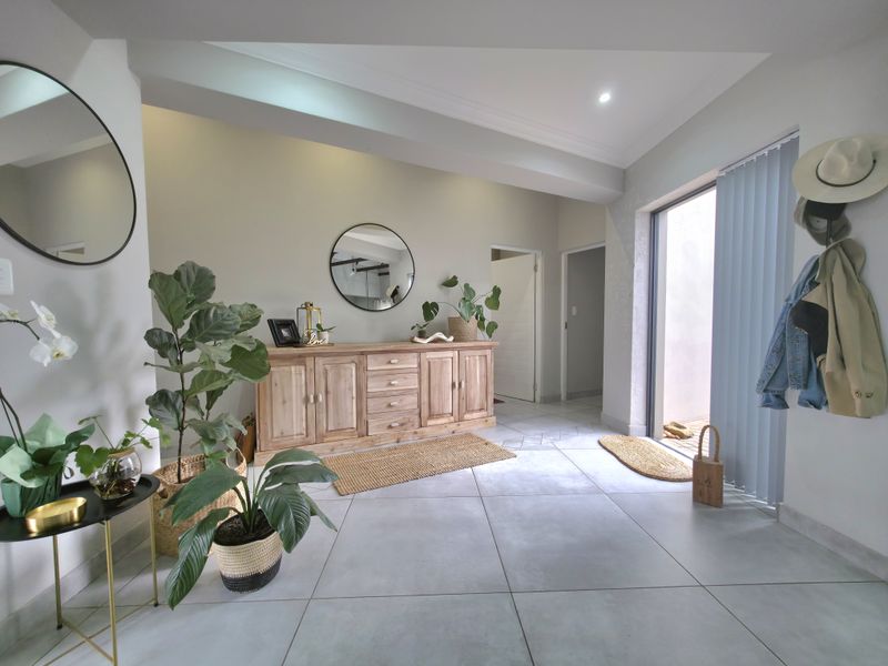 A bright and welcoming entrance hall featuring large format floor tiles, recessed lighting, and direct access to an outdoor area through a sliding glass door.