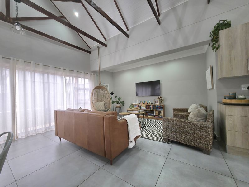 Spacious open-plan living area featuring high vaulted ceilings with exposed timber trusses and modern tiled flooring, creating a bright and airy atmosphere.