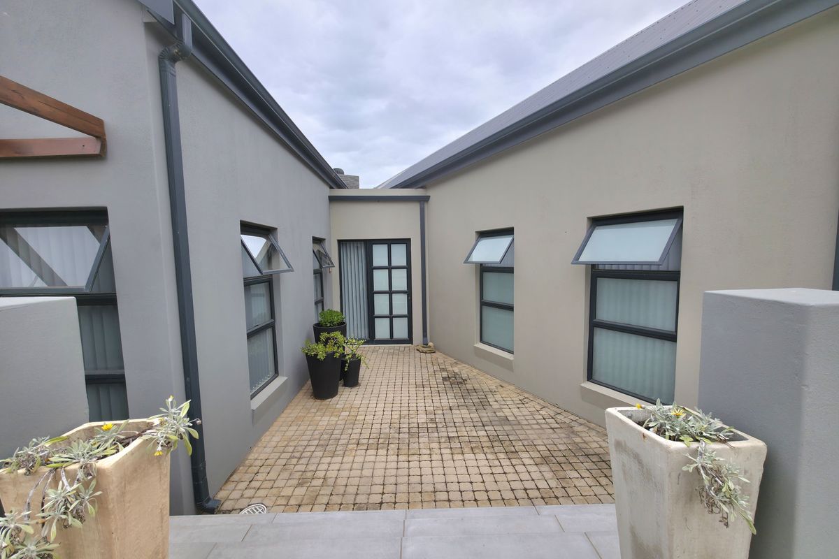A private paved courtyard area connecting two wings of the house, featuring modern grey and beige exterior walls and multiple awning windows.