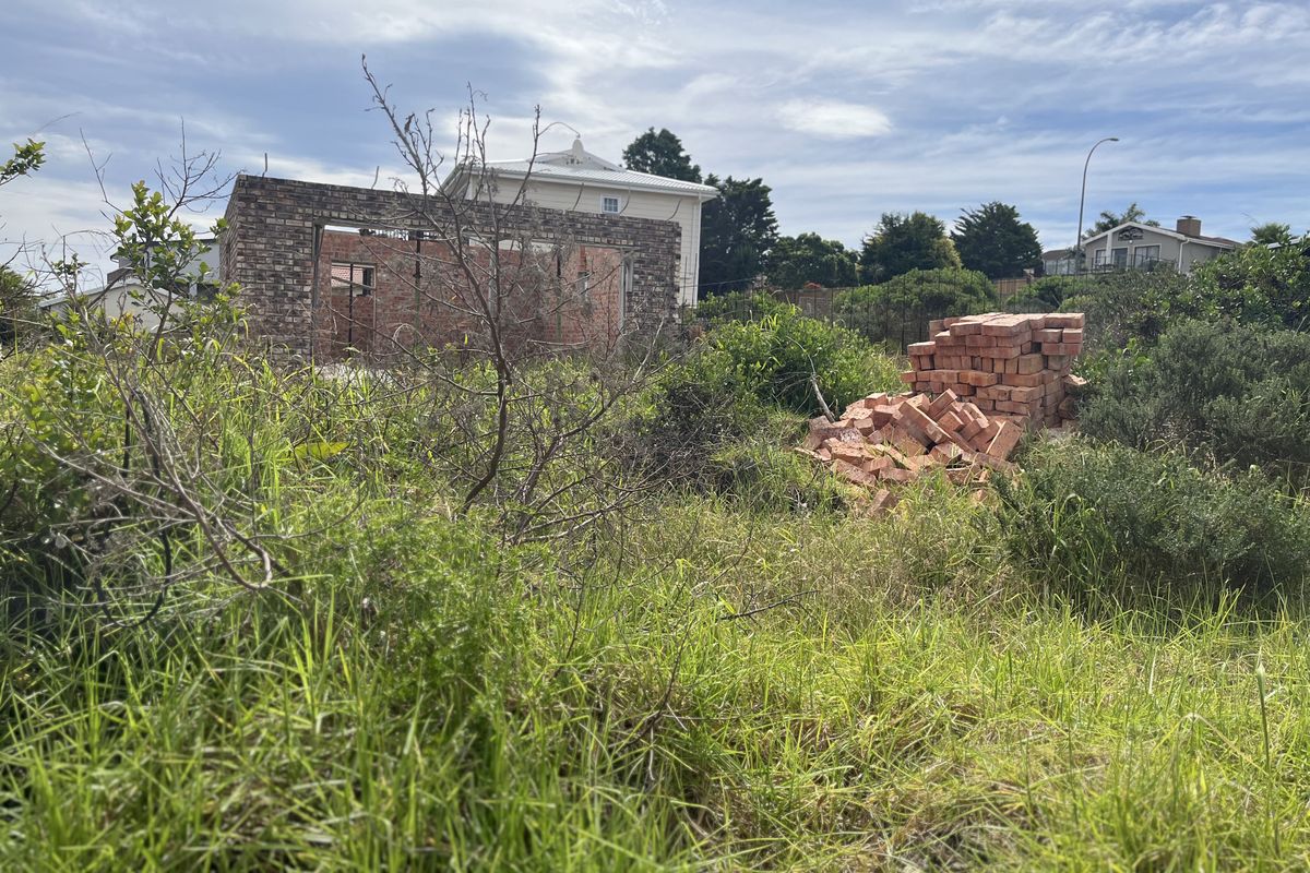 A vacant residential plot featuring overgrown vegetation and an incomplete brick wall structure, offering potential for development.