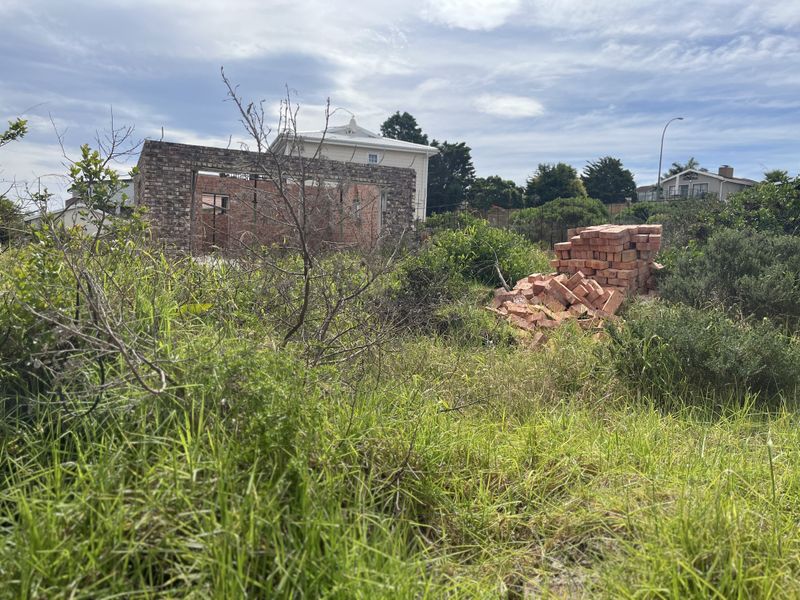 A vacant residential plot featuring overgrown vegetation and an incomplete brick wall structure, offering potential for development.
