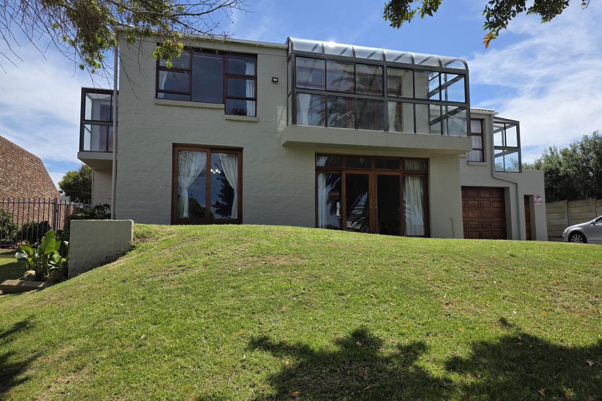 Rear view of a multi-story house featuring a prominent glass-enclosed balcony, sliding doors, and a large sloped lawn area.