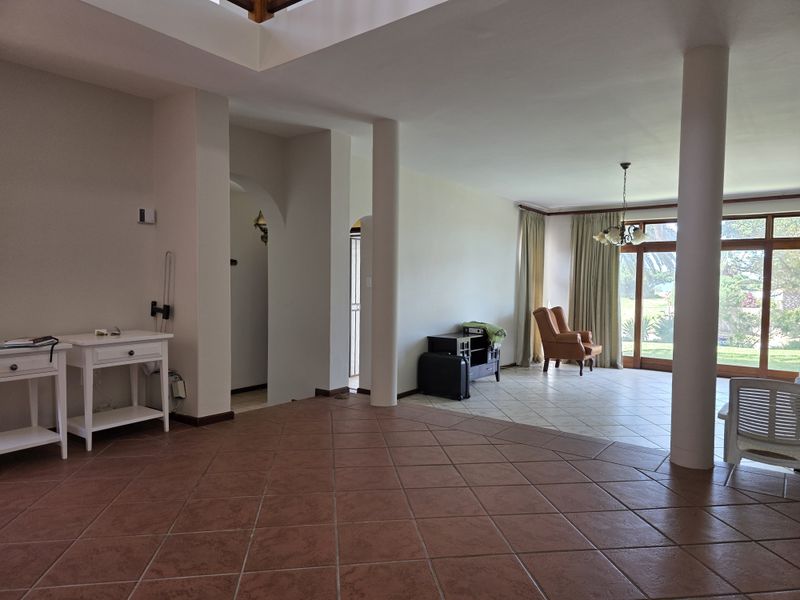 Spacious open-plan living area featuring ceramic tile flooring, structural columns, and large sliding glass doors providing natural light and garden access.