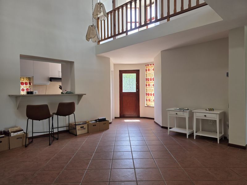 Spacious entrance hall featuring tiled flooring, a mezzanine level with a wooden balustrade, and a convenient pass-through window connecting to the kitchen area.
