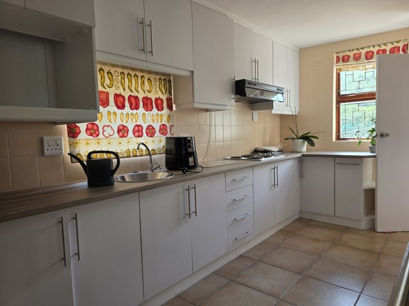 A functional kitchen featuring white cabinetry, laminate countertops, a stainless steel sink, and tiled backsplash with natural light from the window.