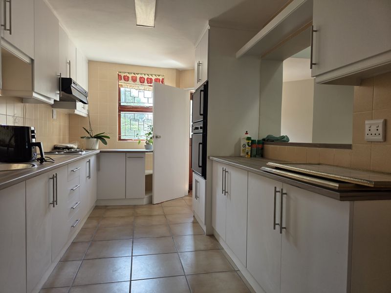 A functional galley-style kitchen featuring white cabinetry, laminate countertops, built-in double oven, and tiled flooring with a window providing natural light.
