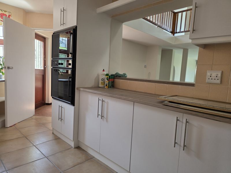 A functional kitchen featuring white cabinetry, laminate countertops, a built-in oven, and a convenient pass-through window overlooking the adjacent living area.