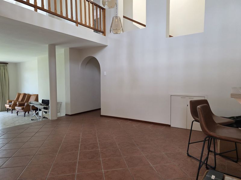 Spacious living area featuring a double-volume ceiling, mezzanine level with wooden balustrade, arched architectural details, and durable tiled flooring.