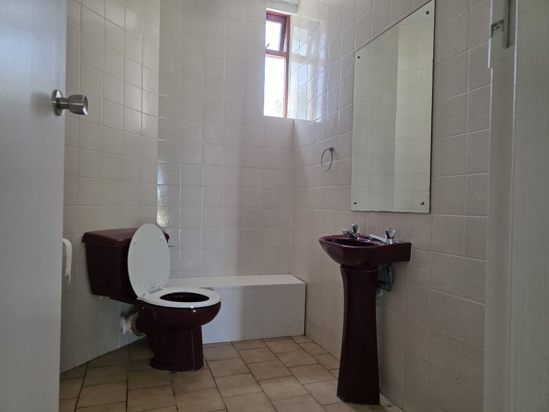 A functional bathroom featuring dated burgundy sanitaryware, full-height wall tiling, and tiled flooring, offering potential for a modern renovation.