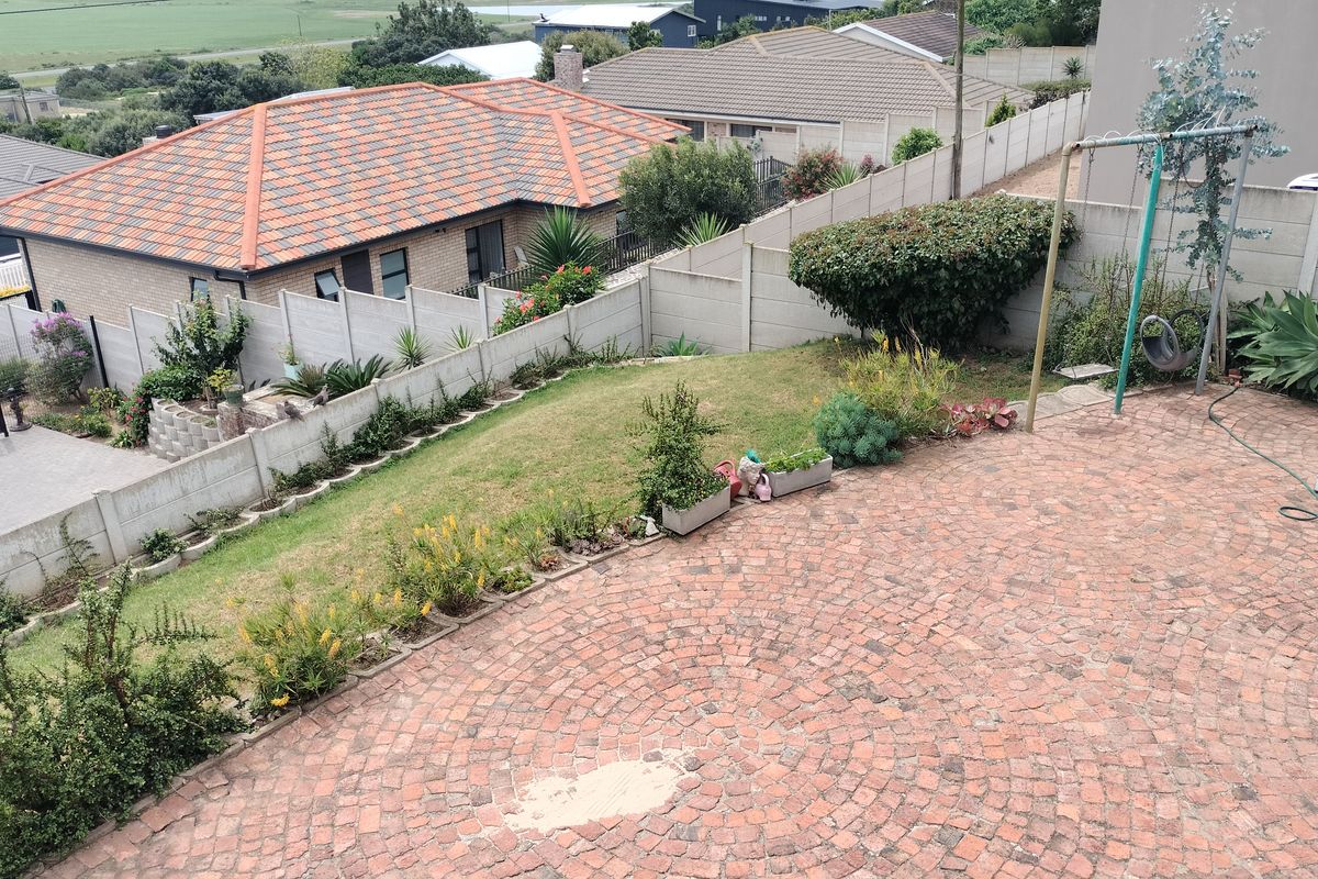 A rear garden featuring a circular brick paved patio area, established lawn, and precast concrete boundary walls.