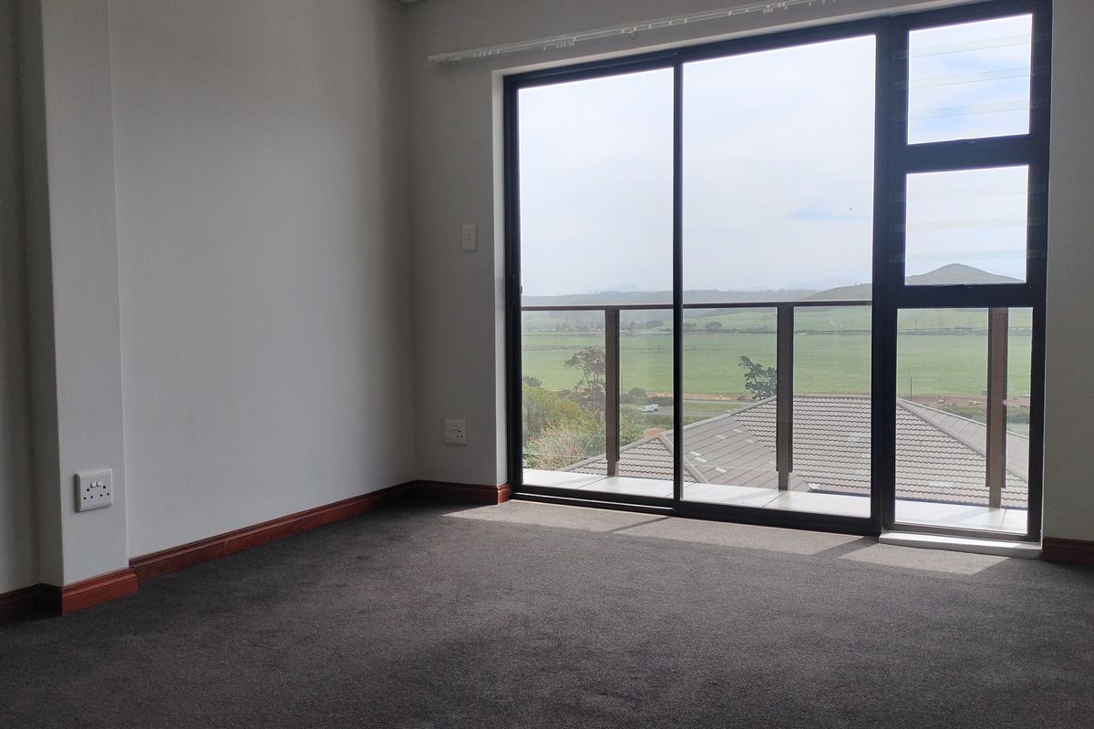 An empty bedroom featuring dark carpeting, neutral walls, and a large sliding glass door that opens to a balcony with scenic landscape views.