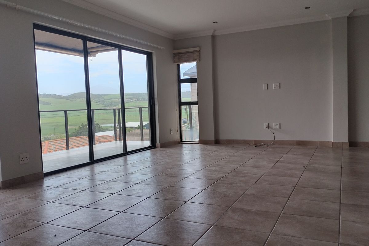 Spacious, empty living area featuring neutral tiled flooring, recessed lighting, and large sliding glass doors that open onto a balcony with scenic views.