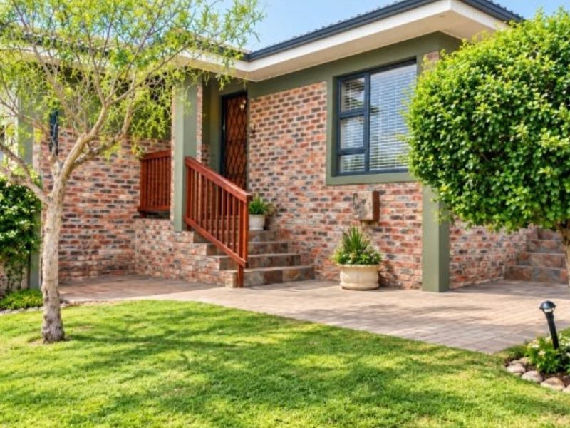 A well-maintained front entrance featuring a face brick facade, paved patio area, and timber handrails leading to the main door.
