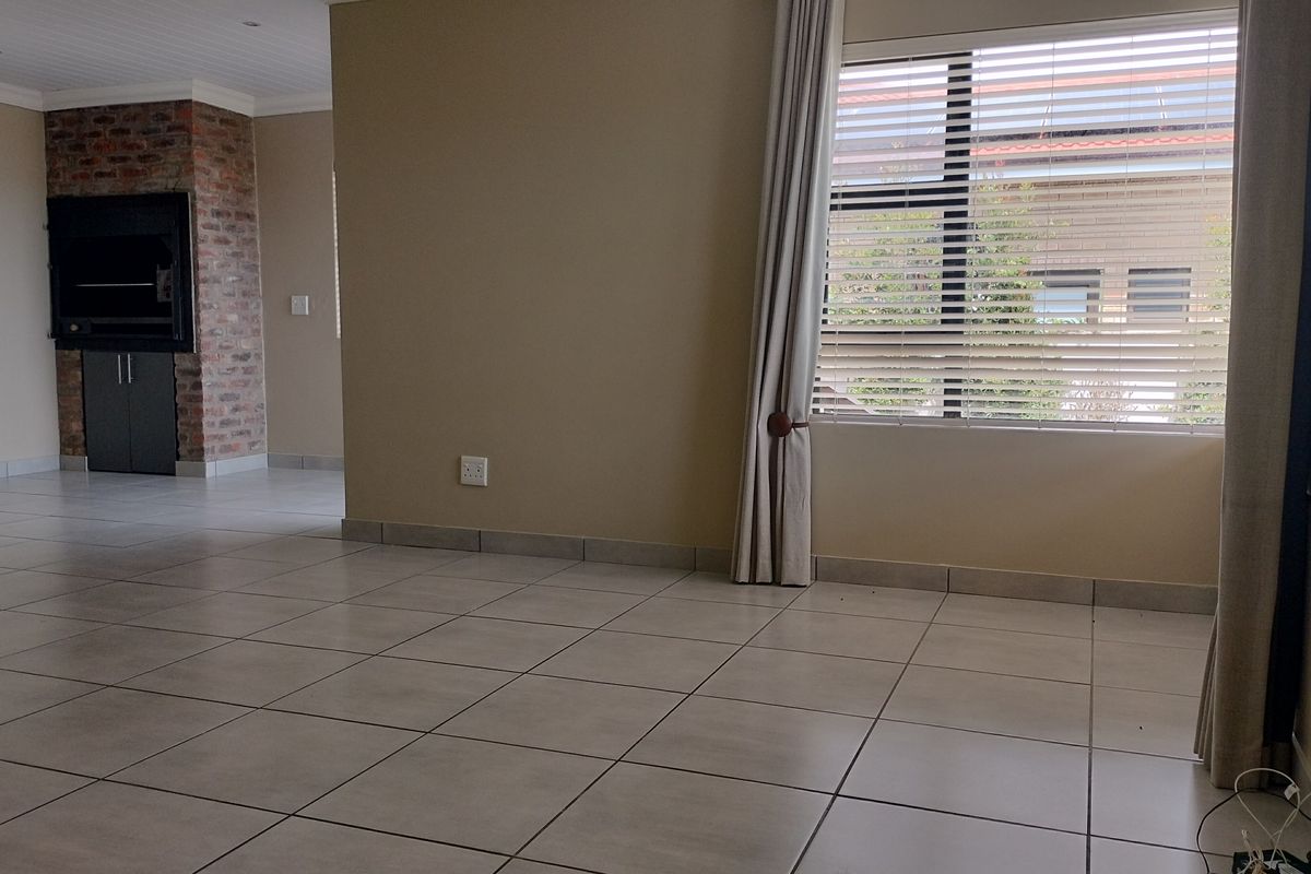Spacious, light-filled living area featuring neutral tiled flooring and a characterful exposed brick built-in fireplace.