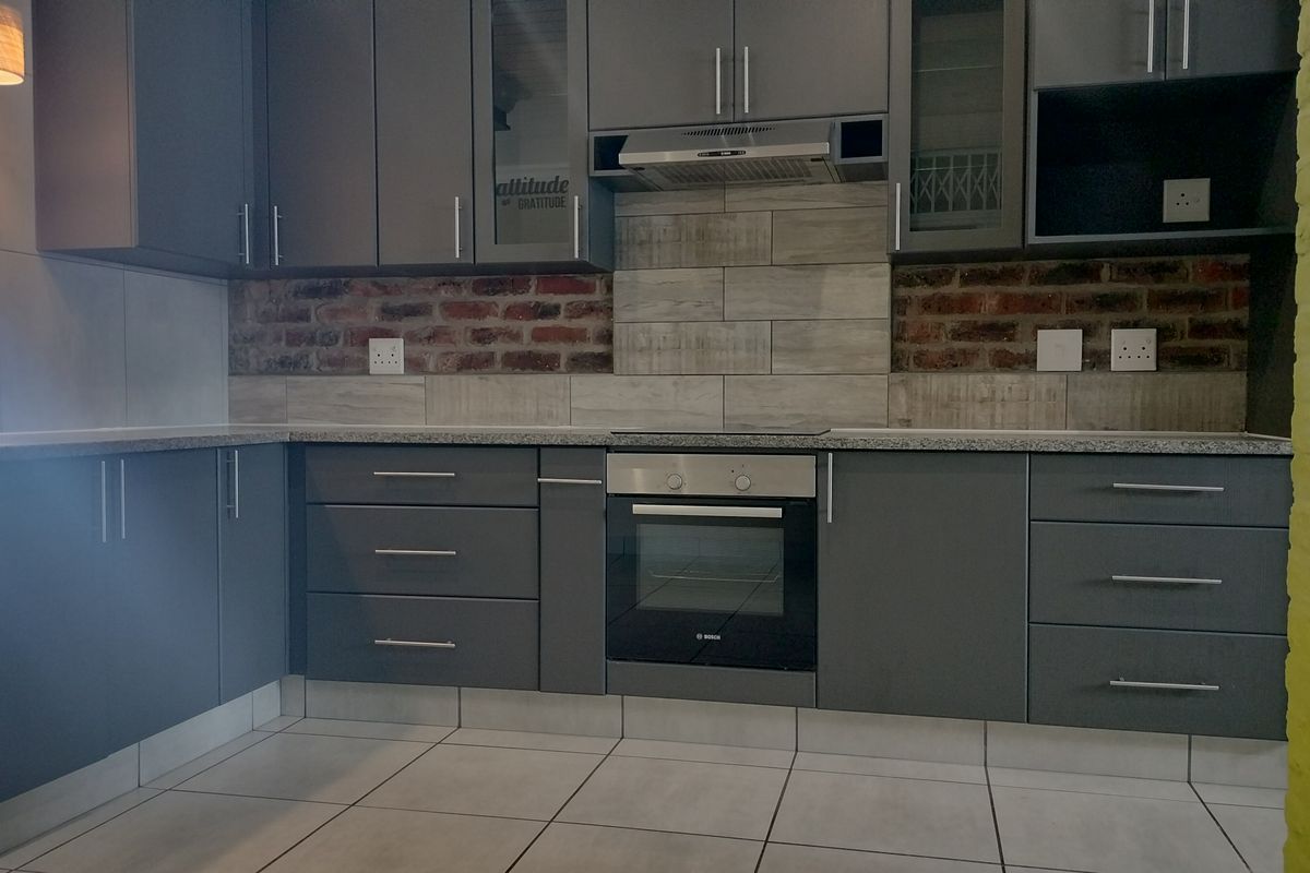 Modern kitchen featuring dark grey cabinetry, built-in oven, extractor fan, granite countertops, and a stylish exposed brick backsplash with tiled flooring.