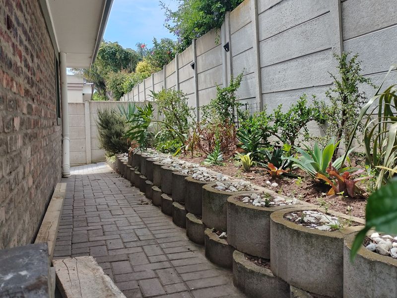 A side garden pathway featuring brick paving, concrete retaining wall planters, and a high precast concrete boundary wall.