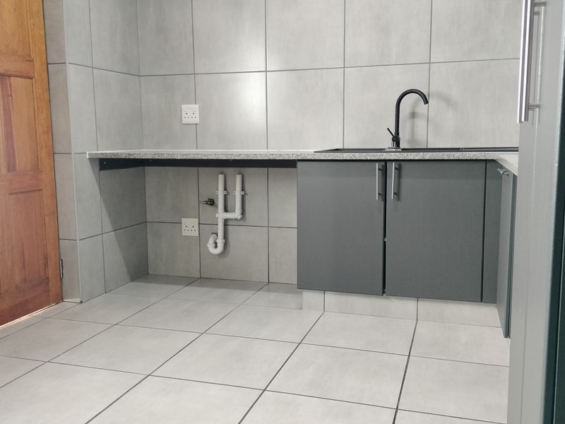 A clean and functional laundry area featuring tiled walls and floors, built-in cabinetry with a stone countertop, and a modern sink fixture.