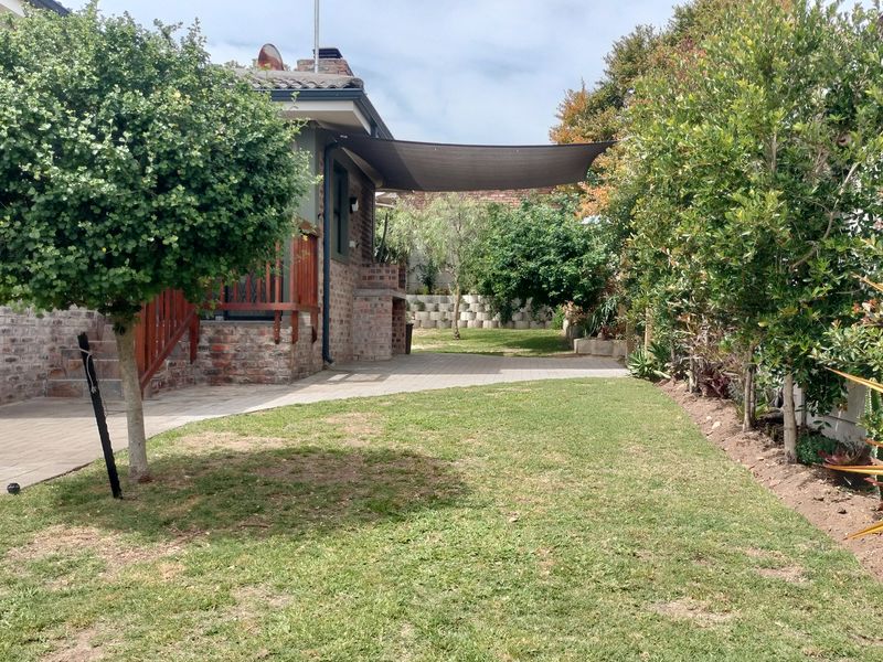 A well-maintained rear garden featuring a paved patio area, a built-in brick barbecue, and a shade sail, perfect for outdoor entertaining.