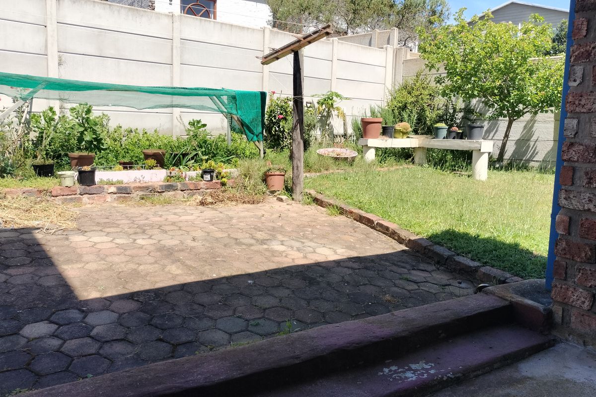 A rear garden area featuring a paved patio, concrete boundary wall, and a built-in concrete bench, offering potential for landscaping and outdoor living improvements.