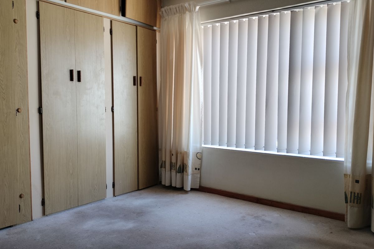 A vacant bedroom featuring built-in wooden cupboards and vertical window blinds, requiring new flooring to refresh the space.