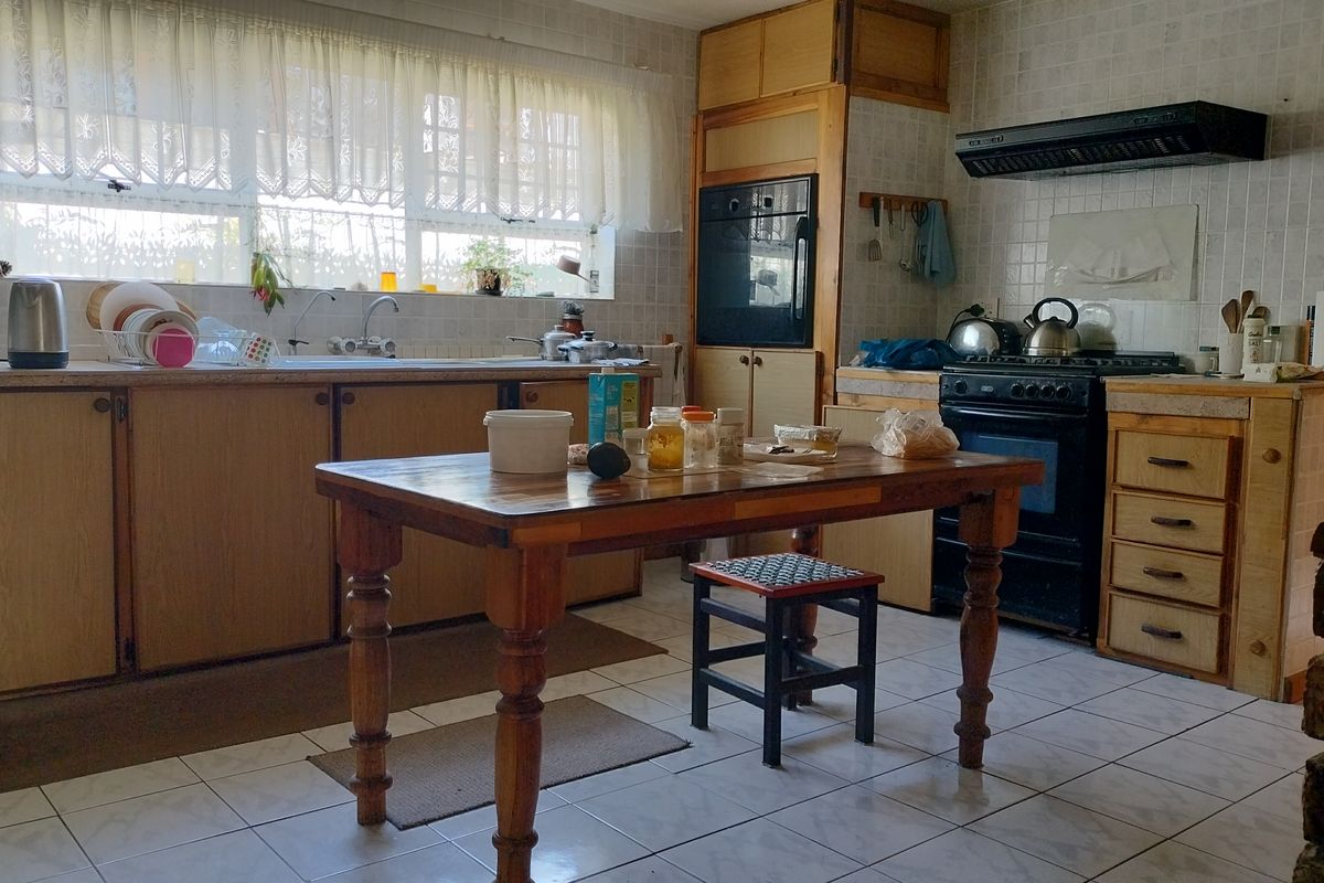 A dated kitchen featuring wooden cabinetry, tiled backsplash, built-in oven, and extractor fan, offering a functional layout with potential for modern renovation.
