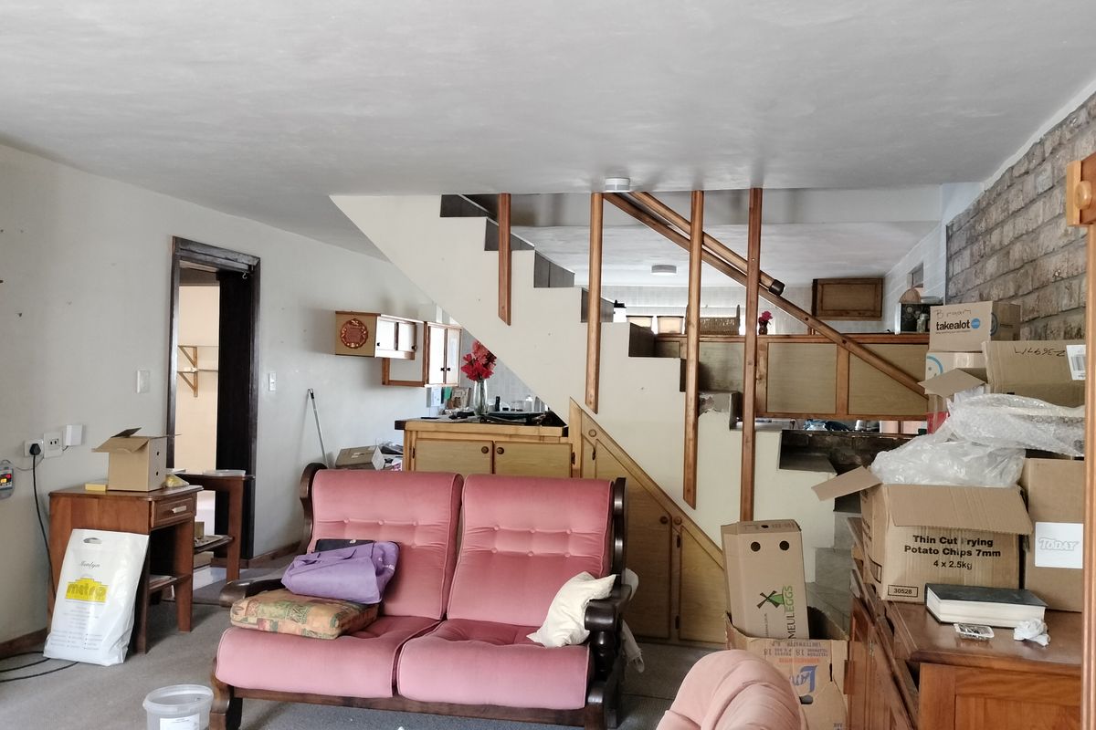 Living area featuring an exposed brick wall and a central staircase with integrated under-stair storage, offering potential for modernization and improved layout.
