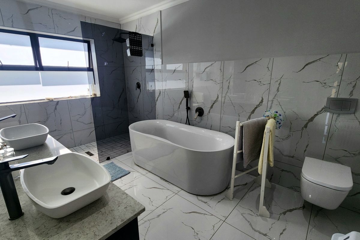 Modern bathroom featuring a freestanding bathtub, walk-in shower, dual vessel sinks on a stone vanity, and wall-mounted toilet with marble-look tiling.