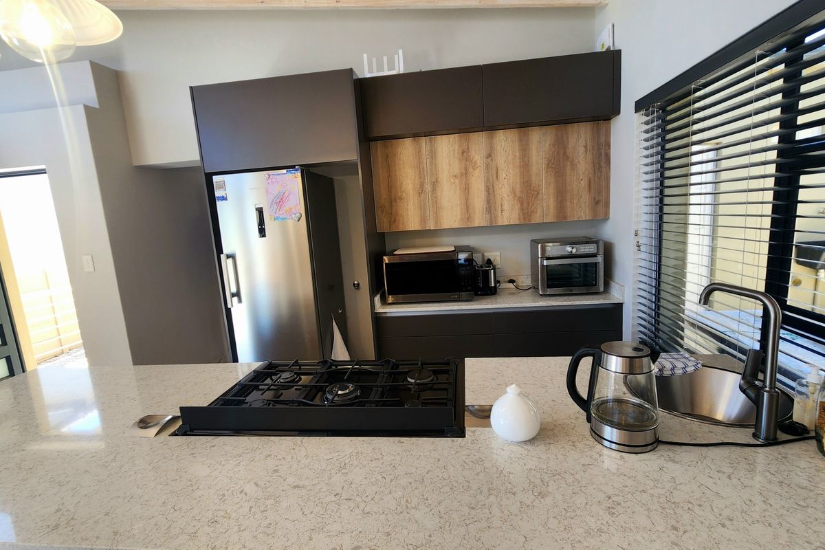 Modern kitchen featuring dark and wood-tone cabinetry, stone countertops, a central gas hob, and an undermount sink with a contemporary mixer tap.