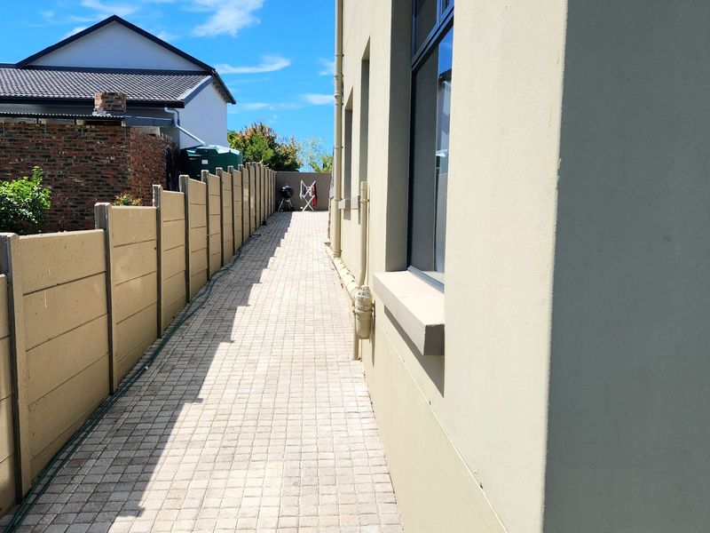 A side walkway featuring paved flooring and a precast concrete boundary wall, providing access along the side of the property.