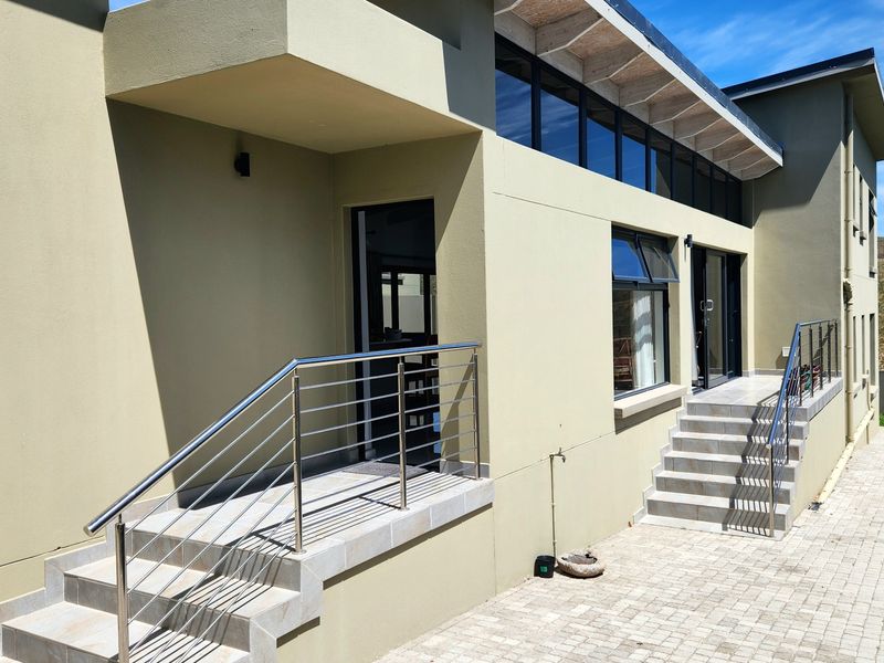 Rear exterior view of the duet property featuring paved patio areas, tiled stairs with stainless steel balustrades, and modern clerestory windows.