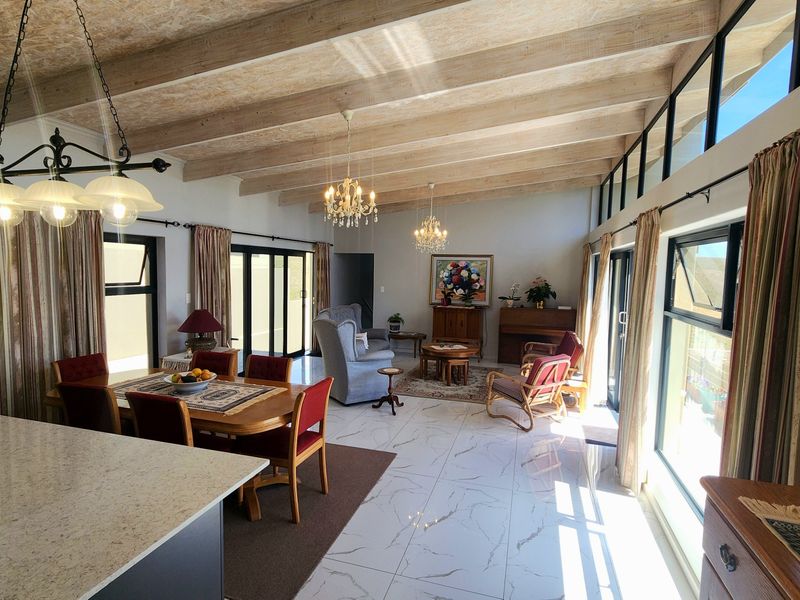 Spacious open-plan living and dining area featuring high exposed timber beam ceilings, large windows, and modern marble-look floor tiles with abundant natural light.