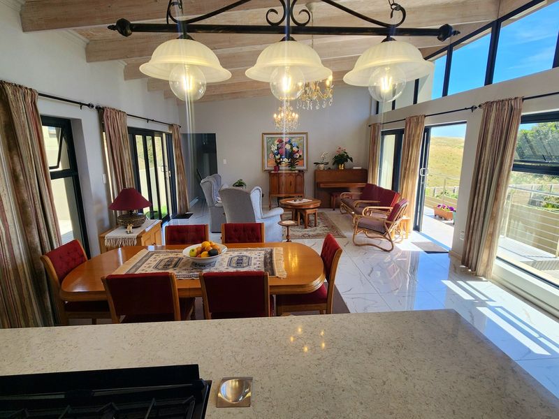 Spacious open-plan living and dining area featuring exposed timber beams, large format tiles, and expansive sliding glass doors leading to an outdoor patio.