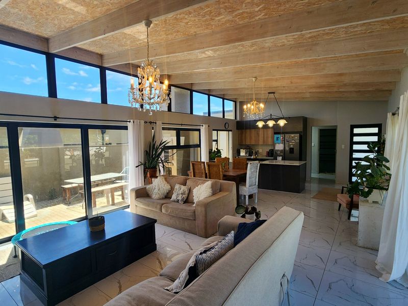 Spacious open-plan living and kitchen area featuring high exposed timber beam ceilings, large format marble-look floor tiles, and expansive glass sliding doors to the patio.