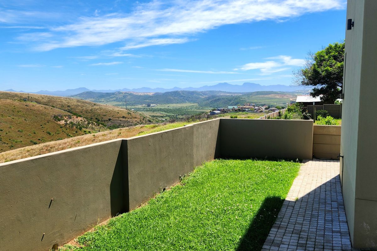 A rear exterior view featuring a manicured lawn, paved walkway, and a retaining wall overlooking scenic mountain and valley vistas.