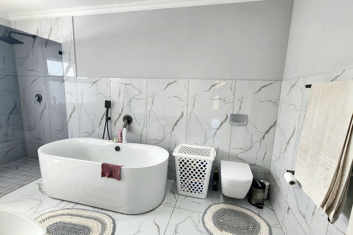 Modern bathroom featuring a sleek freestanding bathtub, a spacious walk-in shower with black fixtures, and elegant marble-look tiling throughout.