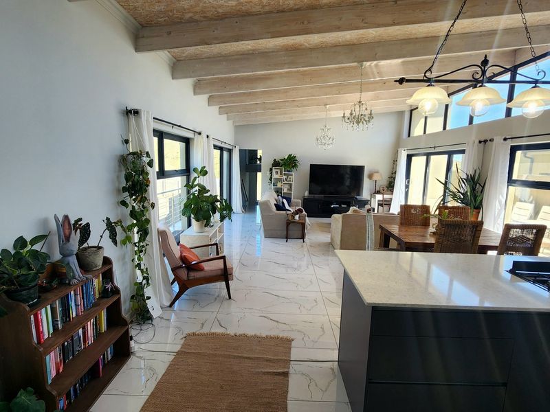 Spacious open-plan living area featuring exposed timber beams, high ceilings, large windows, and a modern kitchen island with a stone countertop.