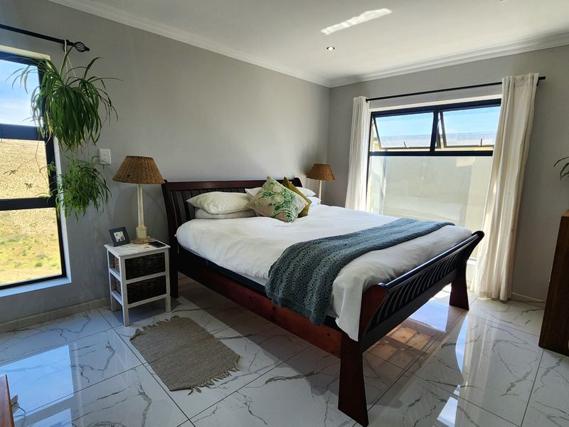 A bright and spacious bedroom featuring modern marble-look tiled flooring, recessed downlights, and large windows providing ample natural light.
