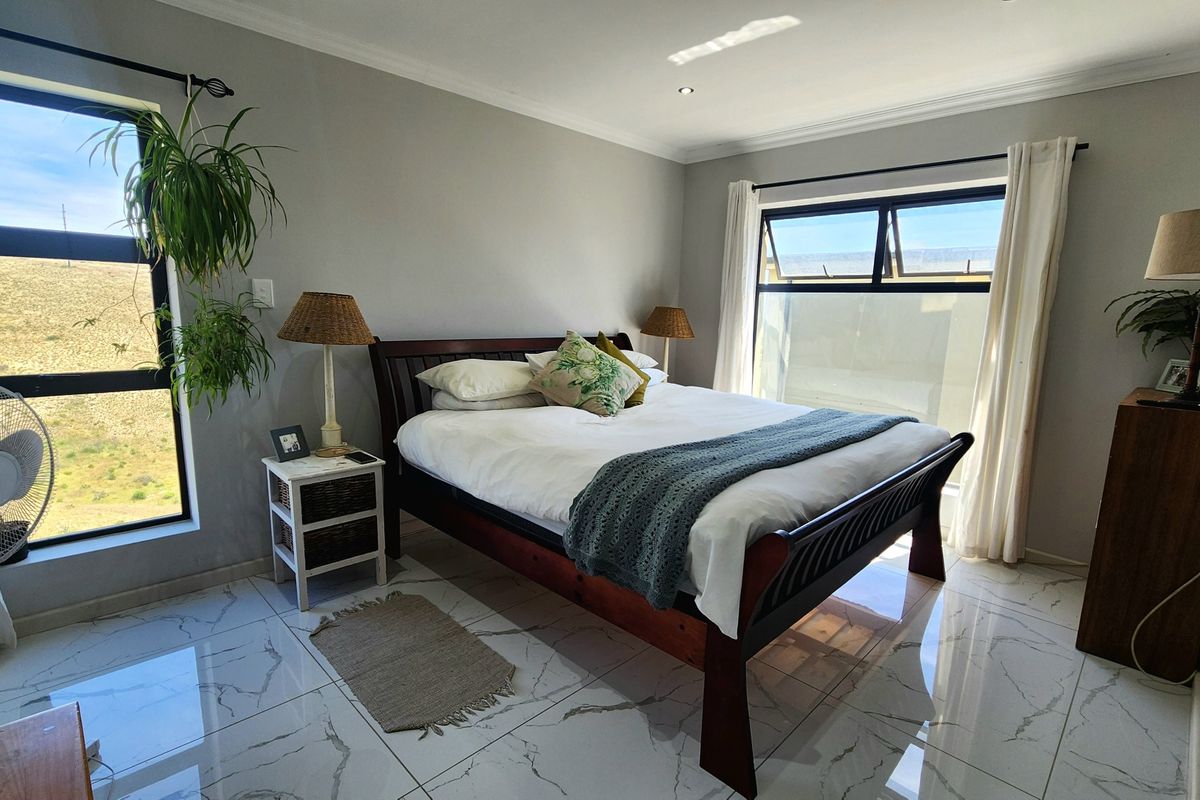 A bright and spacious bedroom featuring modern marble-look tiled flooring, recessed downlights, and large windows providing ample natural light.