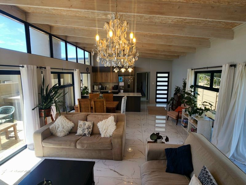 Spacious open-plan living and kitchen area featuring high exposed timber beam ceilings, modern porcelain tile flooring, and large sliding doors leading to outdoor spaces.