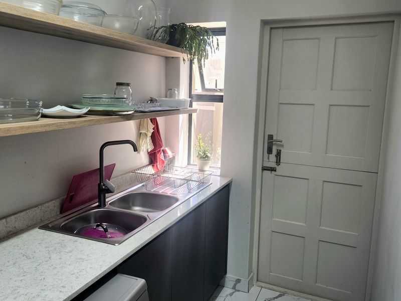 A functional scullery featuring a double basin sink, stone countertops, floating timber shelving, and a classic stable door with tiled flooring.